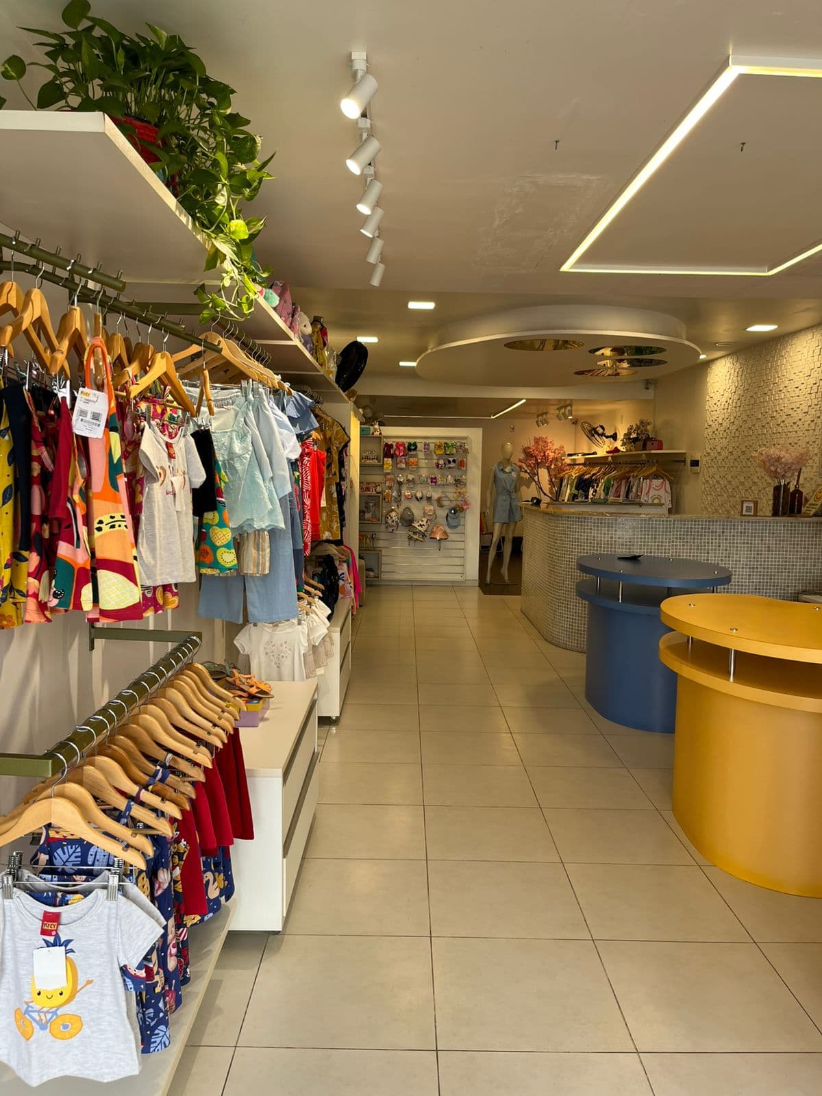 Interior da loja Brulu: araras com vestidos, camisetas e shorts infantis e o balcão de atendimento ao fundo